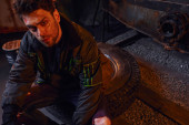 despaired man with scratched unshaven face sitting on tire in darkness of post-apocalyptic subway hoodie #675364484
