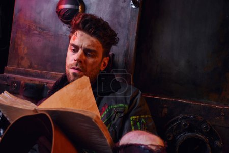 grave homme non rasé lecture livre près rouillé chariot dans le métro abandonné, concept post-apocalyptique