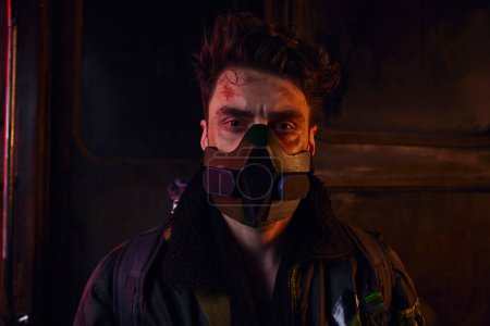 Porträt eines verletzten Mannes mit Gasmaske und abgetragener Kleidung in kontaminierter postapokalyptischer U-Bahn