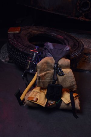 Photo for Backpack with blanket near tire, axe and water bottle in abandoned subway, post-apocalyptic survival - Royalty Free Image