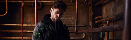 Photo for Depressed man in black dirty jacket near rusty pipes in dark post-apocalyptic subway, banner - Royalty Free Image