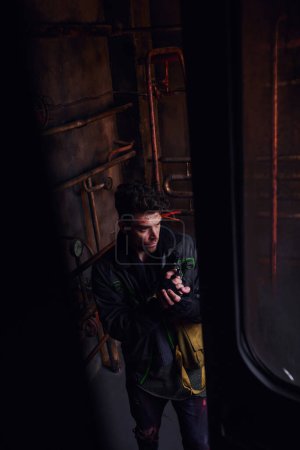 Téléchargez les photos : Vue grand angle de l'homme en vêtements usés debout avec arme dans le tunnel souterrain post-apocalyptique - en image libre de droit