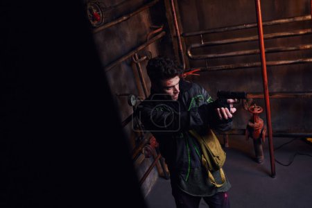 Téléchargez les photos : Homme concentré visant avec arme à feu dans le métro abandonné près de pipelines rouillés, personnage du jeu - en image libre de droit