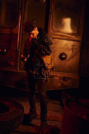 hombre reflexivo mirando a la pieza de repuesto de oxidado vagón de metro en subterráneo post-apocalíptico