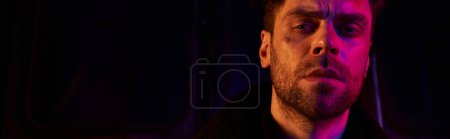 Photo for Man with unshaven injured face looking at camera in red light of post-apocalyptic subway, banner - Royalty Free Image