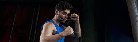 Téléchargez les photos : Homme athlétique assuré en débardeur bleu boxe dans l'obscurité en ville, sport de rue la nuit, bannière - en image libre de droit