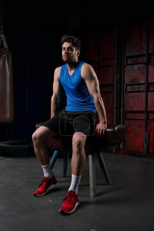Photo for Full length of athletic man in sportswear sitting on sport bench in night city and looking at camera - Royalty Free Image