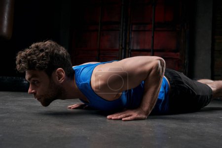 relentless man in blue tank top doing push-ups while working out on city street at night