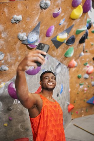Foto de Vertical shot de joven afroamericano hombre t tomando selfie con roca escalada pared fondo - Imagen libre de derechos