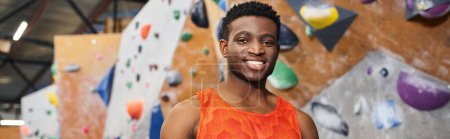 joyful african american man smiling cheerfully at camera with rock climbing wall backdrop, banner
