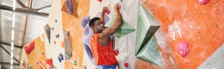handsome african american man in orange shirt climbing up the wall and looking at camera, banner