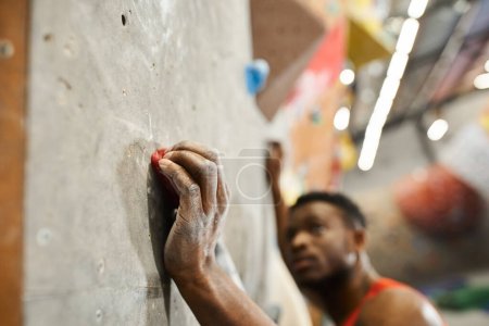 foto borrosa del hombre afroamericano muscular en camisa naranja trepando por la pared de roca, bouldering