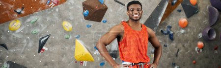 alegre hombre afroamericano posando cerca de la pared de escalada y sonriendo alegremente a la cámara, pancarta