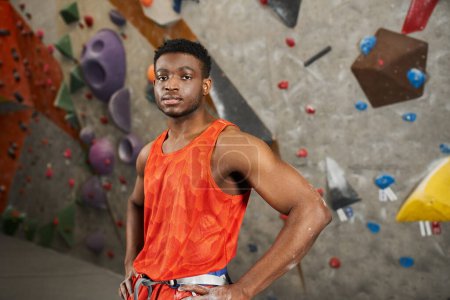 deportivo afroamericano hombre posando en naranja camisa con las manos en las caderas y mirando a la cámara