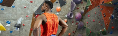 athletic african american male model standing next to climbing rock wall with hands on hips, banner