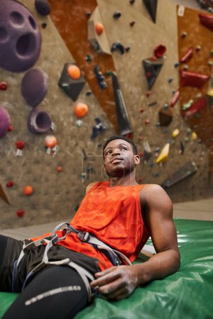 Foto de Tiro vertical del hombre afroamericano relajado después de escalar la pared de roca escalofriante en la almohadilla de choque - Imagen libre de derechos