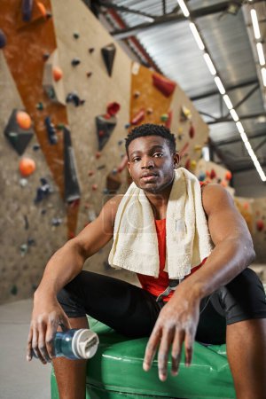 handsome african american man relaxing on crash pad and looking at camera after climbing rock wall