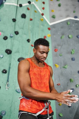 Foto de Tiro vertical del hombre afroamericano muscular usando tiza de gimnasio con pared de cantos rodados en el telón de fondo - Imagen libre de derechos
