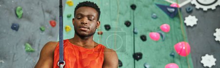 Photo for Handsome sporty african american man posing with safety rope next to climbing wall, banner - Royalty Free Image