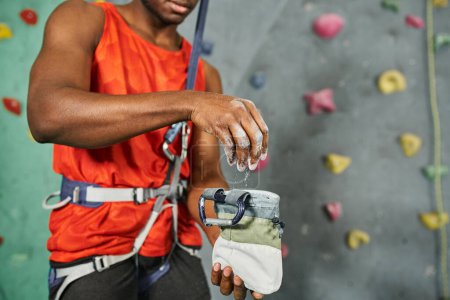 vista recortada del hombre afroamericano usando tiza de gimnasio en su equipo de escalada, bouldering