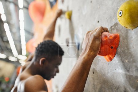 foto borrosa de un joven afroamericano en topless trepando por la pared de bouldering y mirando hacia abajo