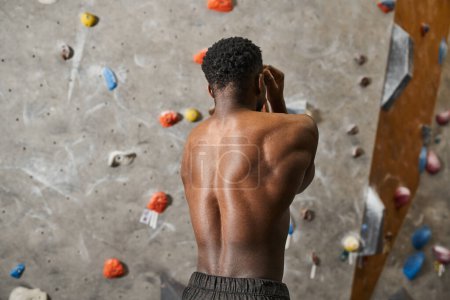 good looking topless african american man flexing his muscles posing next to climbing wall