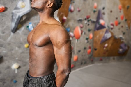 cropped view of sporty young african american man with his shirt off posing near bouldering wall