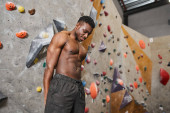 joyful muscular african american man in black pants posing topless next to bouldering wall Mouse Pad 675371178