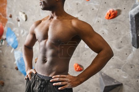 cropped view of fit topless african american man with hands on his hips posing next to rock wall