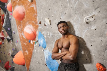muskulöser afrikanisch-amerikanischer Mann posiert oben ohne mit verschränkten Armen auf der Brust neben Kletterwand