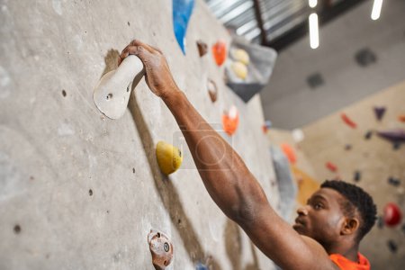 close up of handsome african american man gripping on boulders while climbing up rock wall