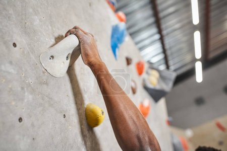 cropped view of hand of sporty african american man gripping on boulders while climbing up wall