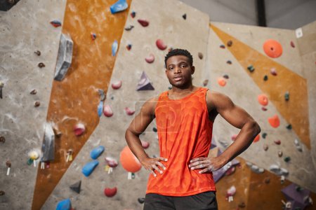 gut aussehender junger afrikanisch-amerikanischer Mann in orangefarbenem Hemd posiert mit den Händen auf den Hüften und blickt in die Kamera