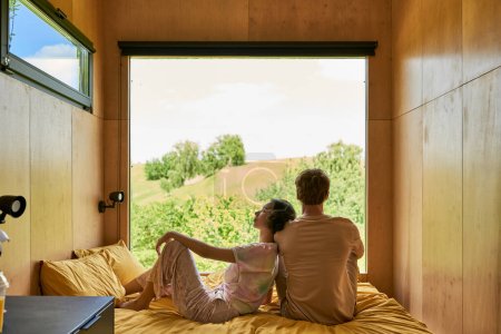 asian woman sitting on bed and leaning on shoulder of boyfriend, relaxing together in country house
