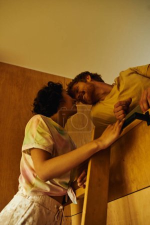 Photo for Happy asian woman climbing wooden ladder of bunk bed near redhead boyfriend, weekend getaway - Royalty Free Image