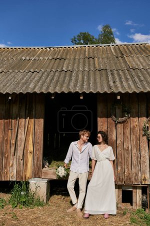 Foto de Concepto de boda rústico interracial recién casados en gafas de sol y vestido de novia cerca de granero de madera - Imagen libre de derechos