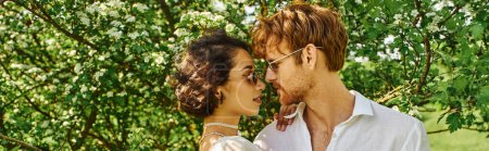 Photo for Young multiethnic couple in sunglasses and white attire hugging in countryside, boho style, banner - Royalty Free Image