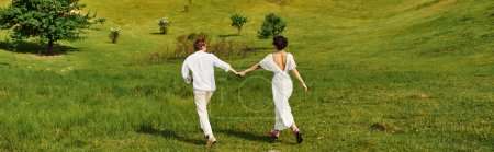 jeunes mariés tenant la main et courant dans le champ vert, mariée et marié en robe de mariée, bannière