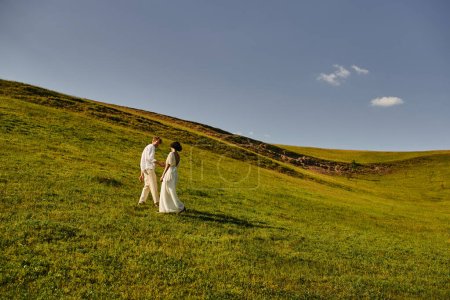 beautiful landscape, just married couple walking in green field, young newlyweds in wedding gown