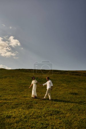 natural landscape, young newlyweds in wedding gown walking in green field, just married couple