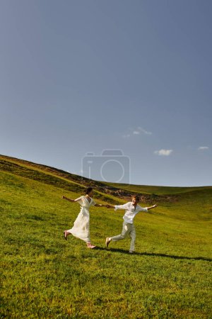 scenic landscape, young newlyweds in wedding gown running in green field, just married couple