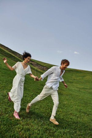 candid photo, happy young newlyweds in wedding gown running in green field, just married couple