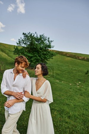 rural nature, happy newlyweds in wedding gown walking together in green field, just married couple