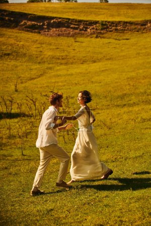 playful interracial newlyweds in wedding attire having fun in green field, rustic wedding