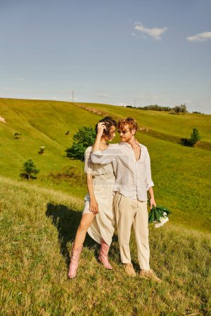junges gemischtrassiges Brautpaar in Boho-Kleidung auf der grünen Wiese, Bindung und Glückseligkeit auf dem Land