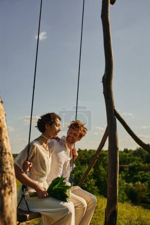young asian bride with flowers swinging with carefree redhead groom, wedding in tranquil countryside
