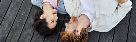 vista superior de la pareja interracial acostado porche de madera y sonriendo el uno al otro al aire libre, pancarta