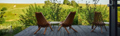 wooden chairs and coffee table on porch with view on scenic landscape near glass building, banner magic mug #675568044