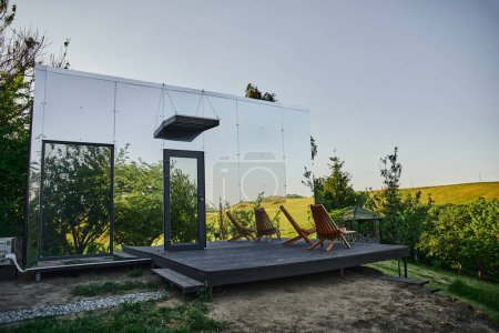 contemporary glass house with wooden porch near green hills in picturesque countryside