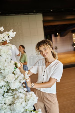 équipe de décorateurs créatifs organisant décor floral dans la salle d'événements spacieuse moderne, design festif